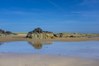 Rock formation reflected in the wet sand on a sunny day at rhosneigr beach, anglesey, uk