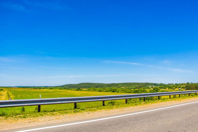 Road amidst field against blue sky