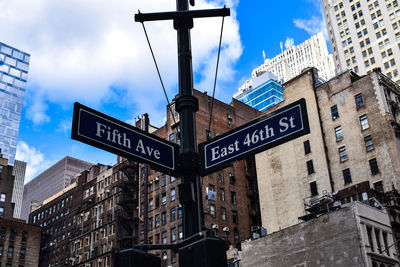 Low angle view of road sign by buildings against sky