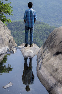 Rear view of man standing on mountain with reflection in puddle