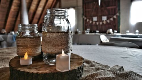 Lit candles by decorated glass jar on wood