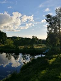 Scenic view of field by lake against sky