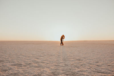 Rear view of woman walking at beach against clear sky