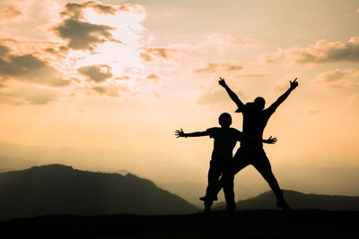 Silhouette woman with arms raised standing against orange sky