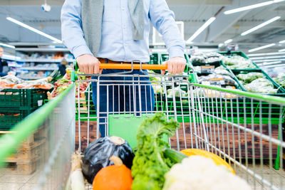 Man shopping in supermarket pushing his trolley with vegetables and groceries