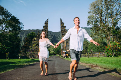 Couple running on footpath at gate against sky