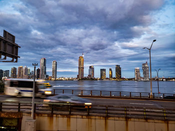 Illuminated buildings by street against sky at dusk