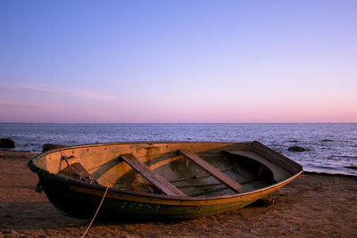 Abandoned boat on beach against sky during sunset