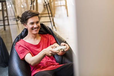 Happy young man playing video game while sitting on bean bag at home