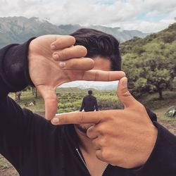 Man making frame with person sitting against landscape