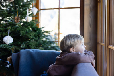 Cute little boy looking out the wooden window in a cosy chalet. christmas holidays concept