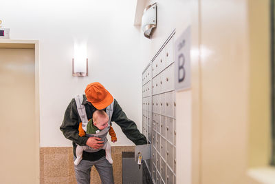 Father carrying daughter in carrier opening locker in room while during pandemic