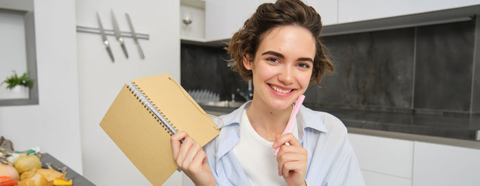 Portrait of young woman using mobile phone while standing in office