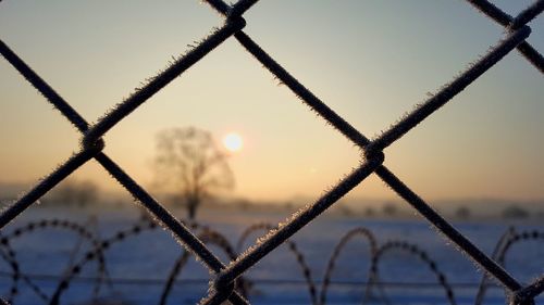 Close-up of chainlink fence against sky during sunset