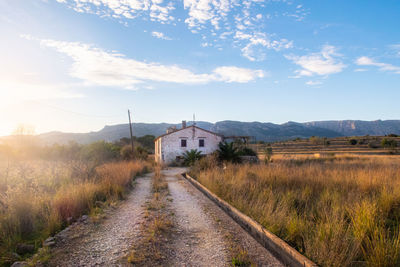 Country house with dirt road at sunset.