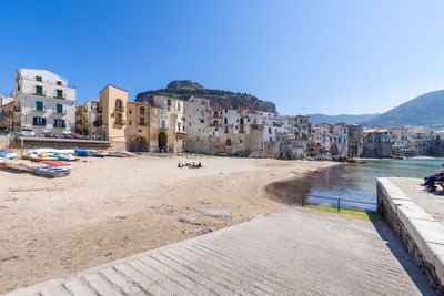 Buildings by sea against clear blue sky