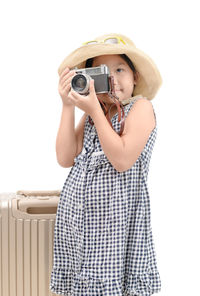 Girl photographing with camera by suitcase against white background