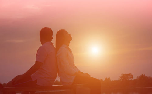 Couple sitting on rock against sky during sunset