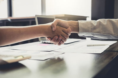 Cropped hands of business people shaking hands at desk in office