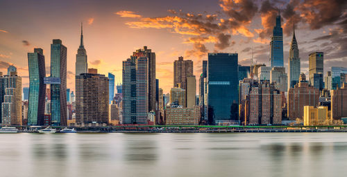 Sea by modern buildings against sky during sunset