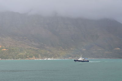 Boat sailing in river against mountains during foggy weather on sunny day