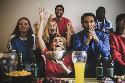 Male and female soccer fans watching match while sitting on sofa at home