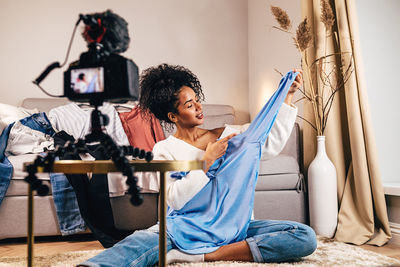 Camera recording woman holding dress while sitting on rug at home