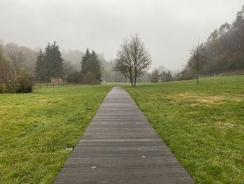 Empty footpath amidst field against sky