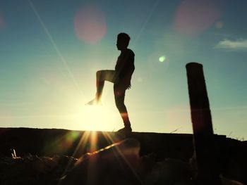 Silhouette man standing on rock against bright sun