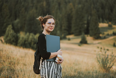 Happy woman freelancer with glasses working on laptop, remote location in nature