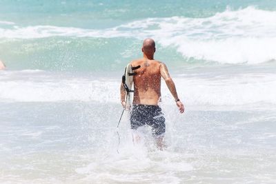 Rear view of man with arms raised on beach