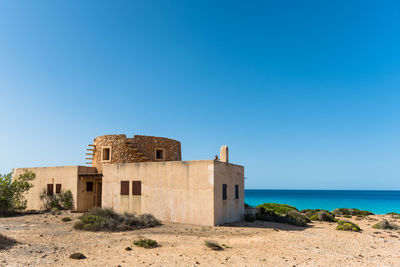 Built structure by sea against clear blue sky