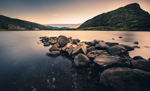 Rocks by sea against sky during sunset