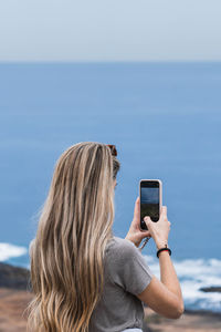 Side view of woman photographing with camera against sky