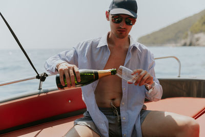 A young guy pours champagne while sitting in a boat at sea.