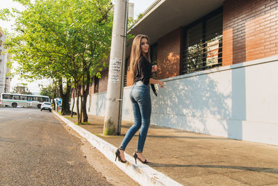 Portrait of young woman standing on footpath against built structure in city