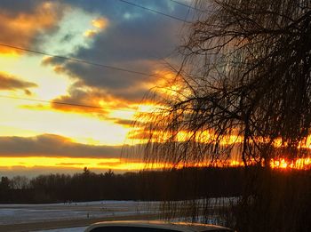Silhouette trees on landscape against dramatic sky during sunset