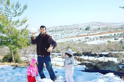 Father playing with daughters in snow against sky