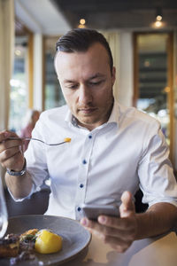 Businessman using mobile phone while eating lunch at restaurant