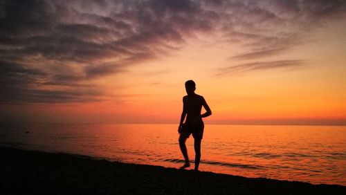 Silhouette man standing on beach against sky during sunset