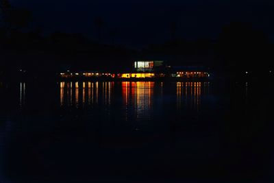 Illuminated buildings by lake against sky in city at night