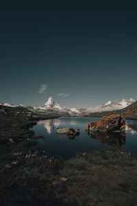 Scenic view of lake by snowcapped mountain against sky during winter