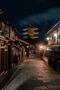 Illuminated street amidst buildings against sky at night