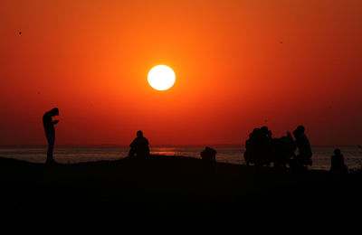 Silhouette people on sea against orange sky