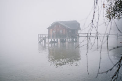 Wooden house by lake against sky