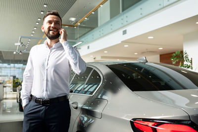 Man talking on smartphone near car in showroom