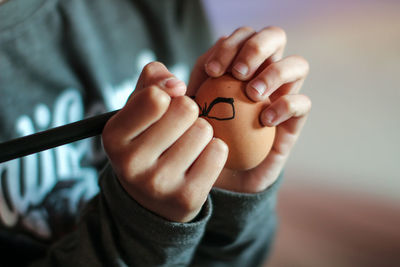 Midsection of kid drawing on brown egg