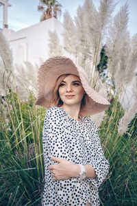 Smiling young woman wearing hat standing against plants outdoors