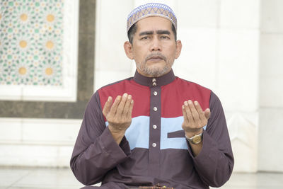 Portrait of mature man praying while sitting at mosque