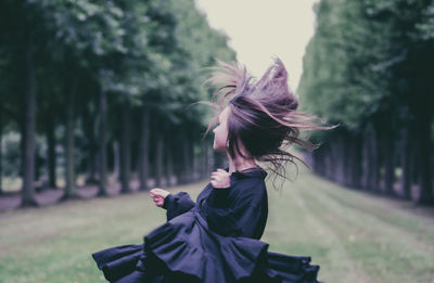 Smiling young woman looking away while standing at park against sky